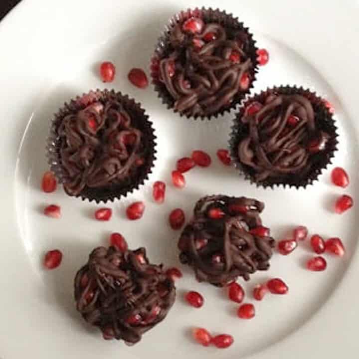 Chocolate pomegranate clusters on a white plate surrounded by pomegranate arils
