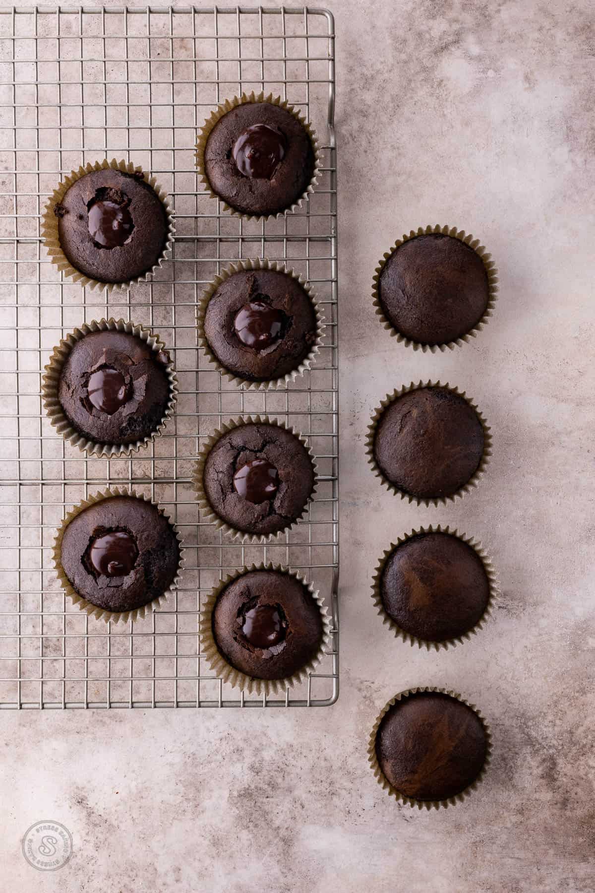 Chocolate cupcakes on a wire rack, with some cored and filled with chocolate ganache