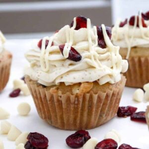 Golden cupcakes topped with creamy swirls of cream cheese icing, dried cranberries and white chocolate drizzle