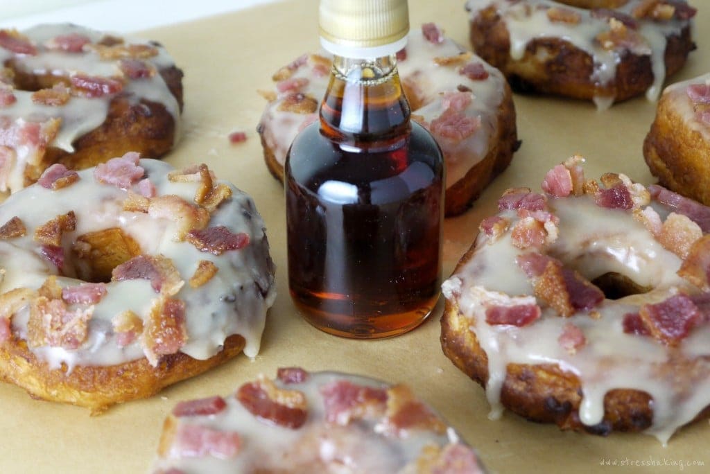 Maple glazed donuts topped with bacon next to a maple syrup bottle