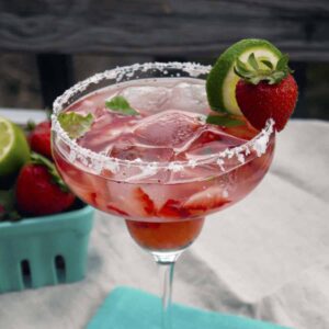 Strawberry basil margarita in a clear margarita glass with a salt rim garnished with a lime wedge and strawberry