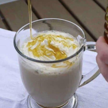 Honey being drizzled on top of a latte in a clear mug