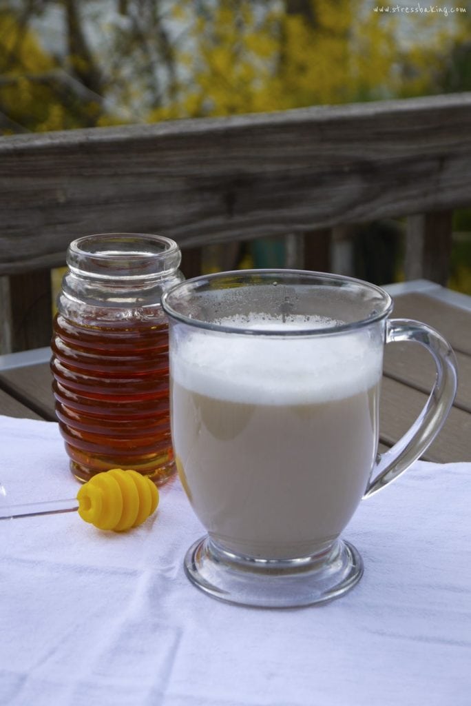 A jar of honey next to a latte in a clear mug