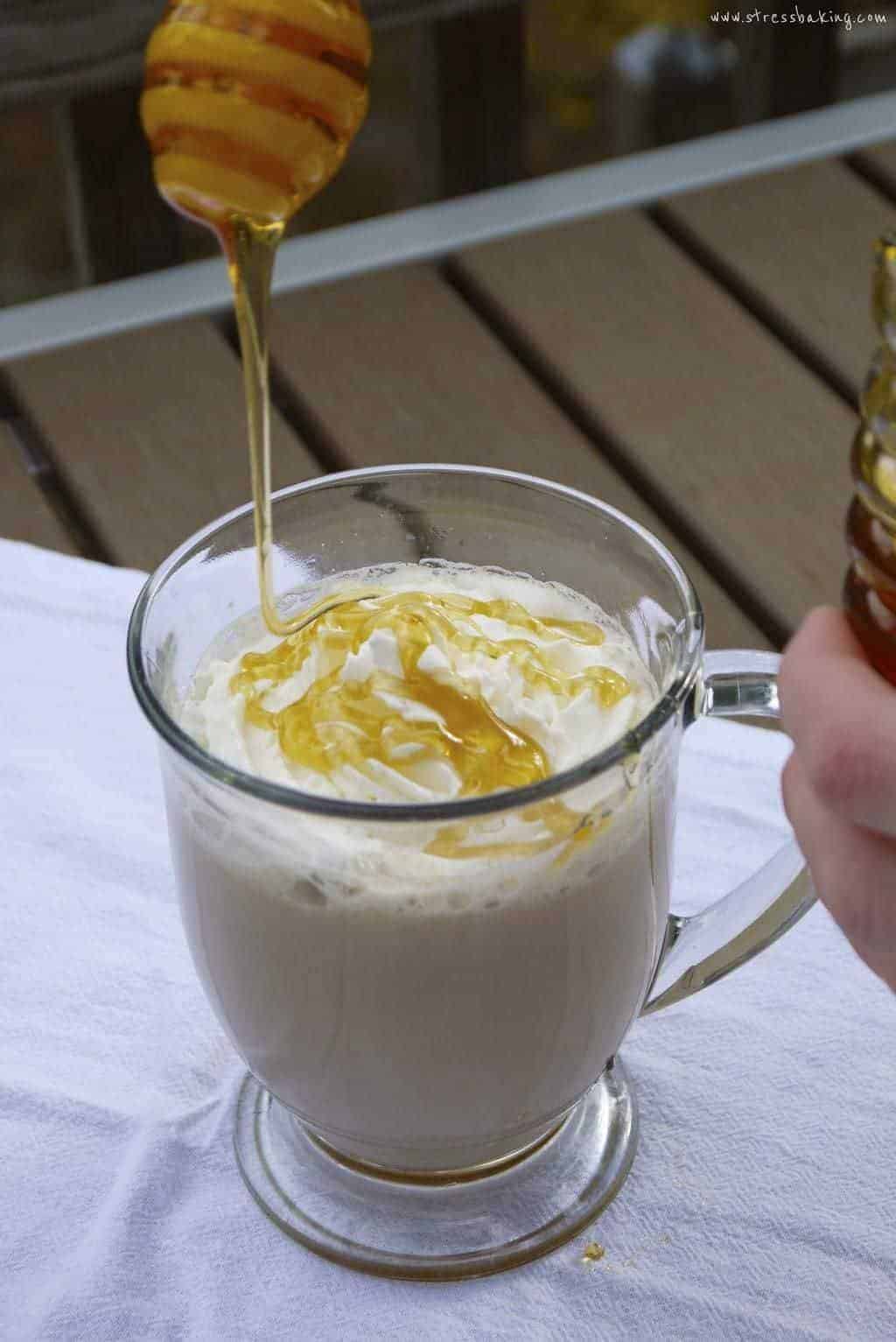 Honey being drizzle onto whipped cream topping a latte in a clear mug