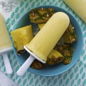 Yellow pineapple popsicle on top of a bowl of sliced pineapple