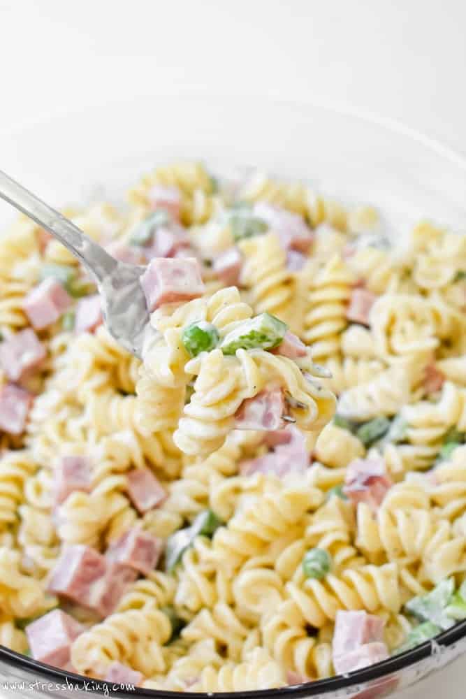 Pasta salad on a fork being held over a bowl of colorful pasta salad