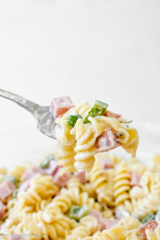 Pastasalade op een vork die boven een kom met kleurrijke pastasalade wordt gehouden