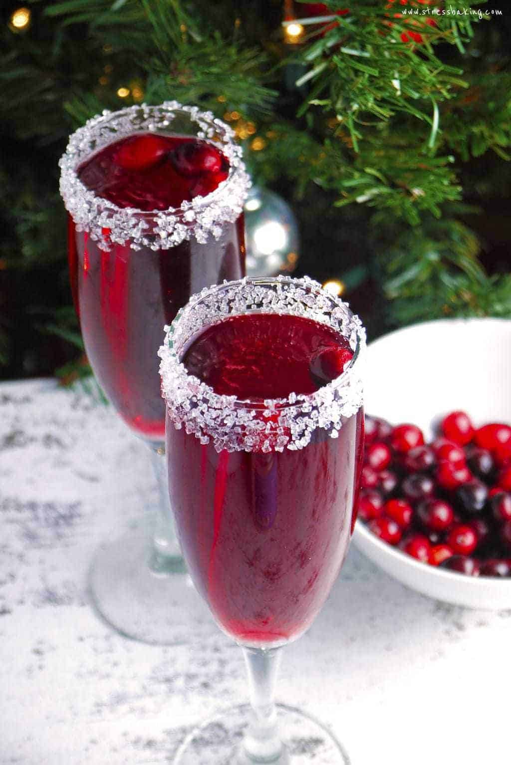 Two glasses of cranberry mimosa in front of a Christmas tree with sugared rims