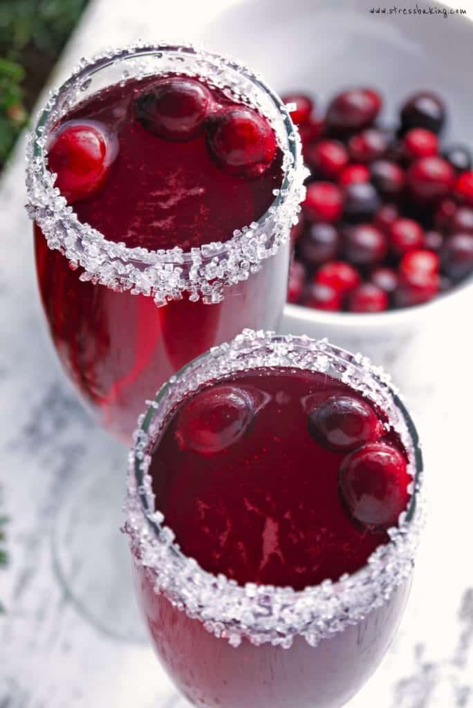 Cranberry Mimosas rimmed with sugar and topped with fresh cranberries next to a bowl of fresh cranberries