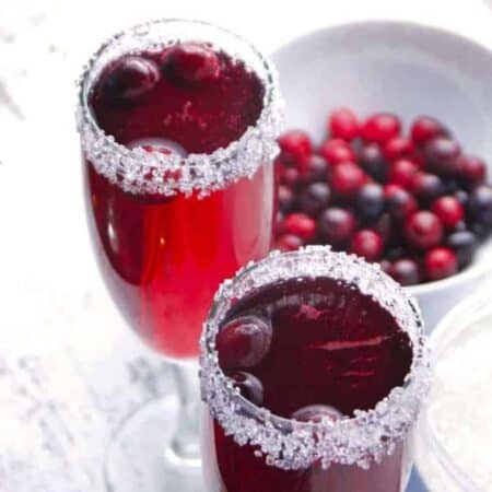 Two glasses of cranberry mimosas with a bowl of cranberries