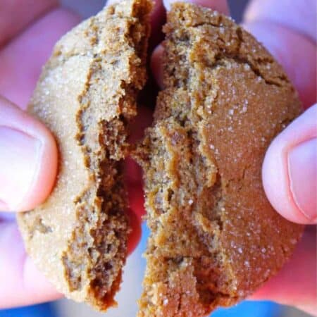 A chewy ginger molasses cookie with a crinkled top being broken in half