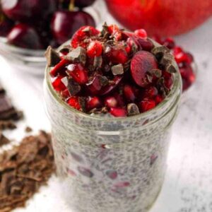 A mason jar full of chia pudding topping with cherries, pomegranate arils and chocolate