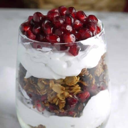 A parfait made of coconut whipped cream, granola and pomegranate arisl