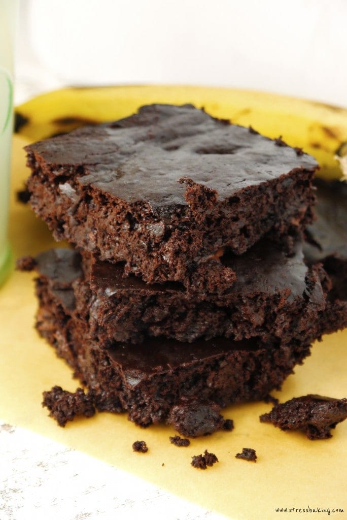 Fudgy Chocolate Banana Brownies stacked on top of parchment paper with a banana