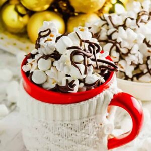 Popcorn covered in chocolate drizzle in a red mug wrapped in a sweater