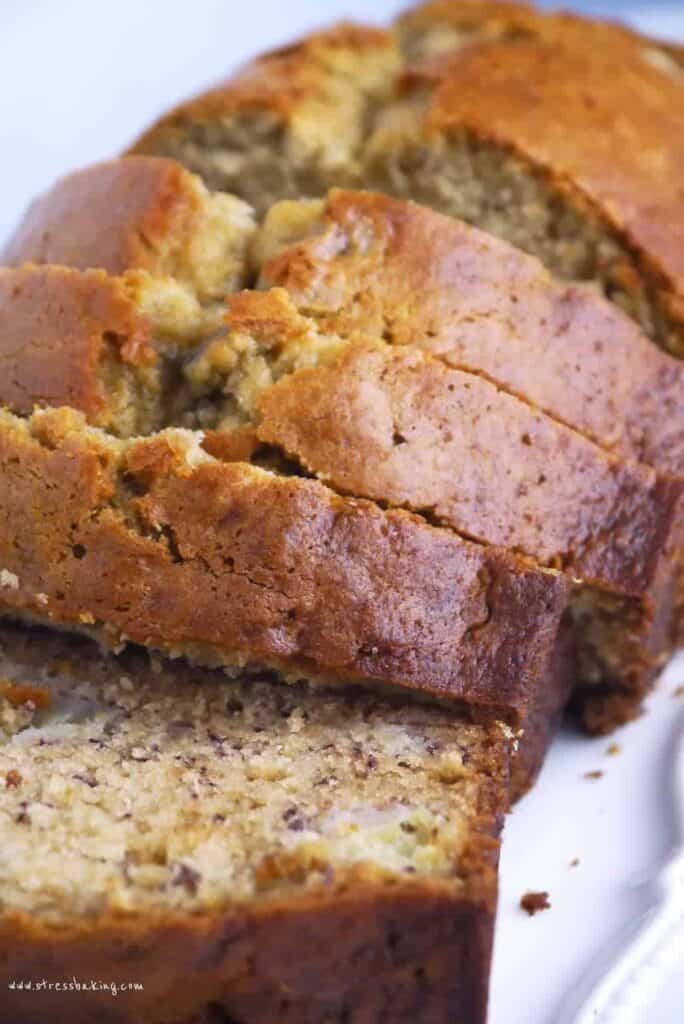 A loaf of golden banana bread, sliced on a white plate