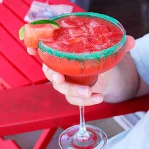 Bright red watermelon margarita with a wedge of watermelon and green sugar rim