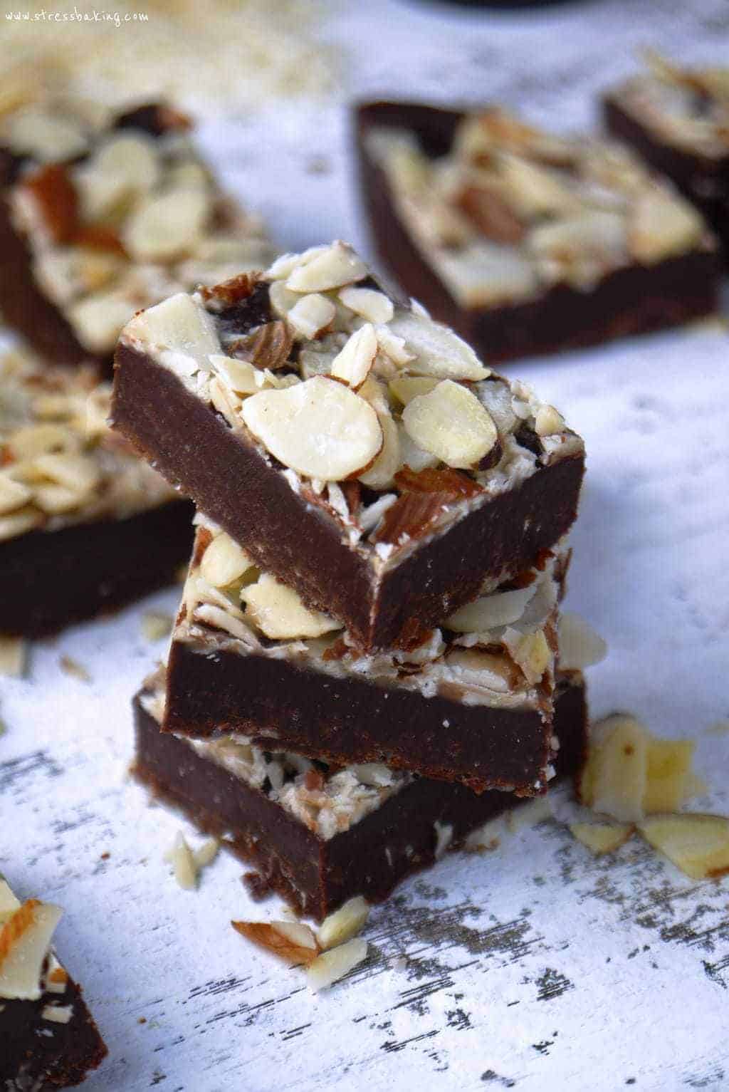 Chocolate fudge stacked on a distressed white surface topped with thinly sliced almonds