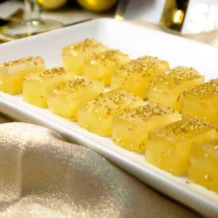 Yellow mimosa jello shots on a white platter and topped with gold sprinkles