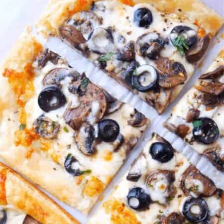 Cheesy pizza topped with black olives and mushrooms on a golden puff pastry crust