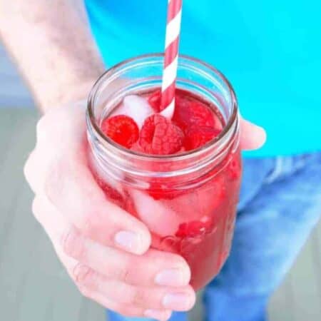 A mason jar full of Raspberry Rosé Sangria with fresh raspberries and a striped straw
