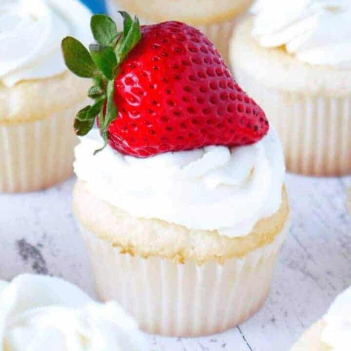 Angel food cupcakes topped with fluffy whipped cream frosting and bright red strawberries
