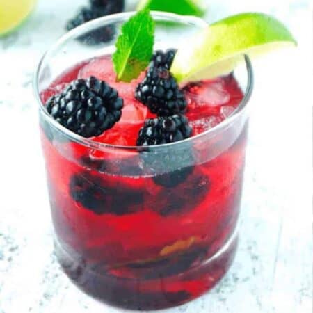 A brightly colored red blackberry mint julep in a glass with fresh blackberries, lime wedge and mint leaf