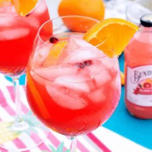 A clear glass full of colorful blood orange sangria with orange slices and pomegranate arils