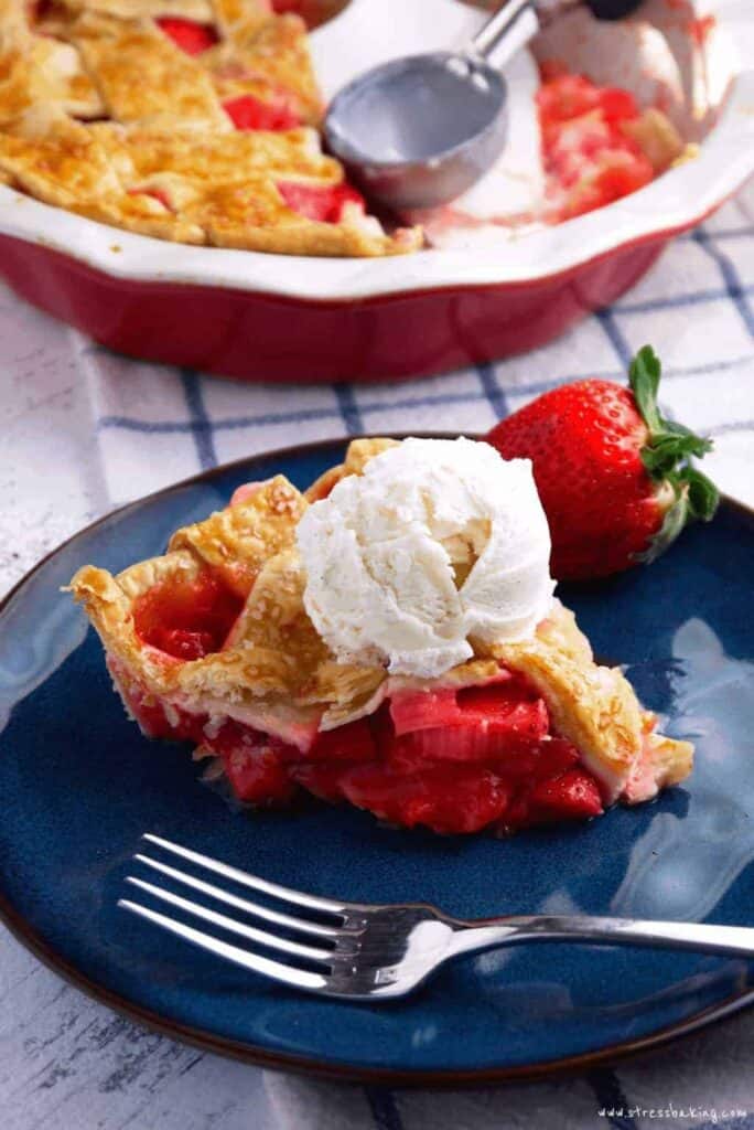 A slice of strawberry rhubarb pie topped with vanilla ice cream on a blue plate