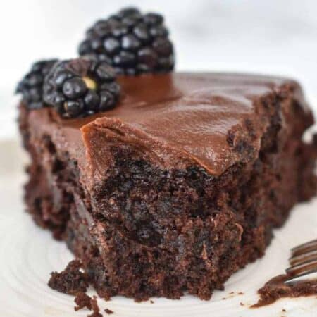 A slice of dark chocolate cake with chocolate frosting topped with blackberries