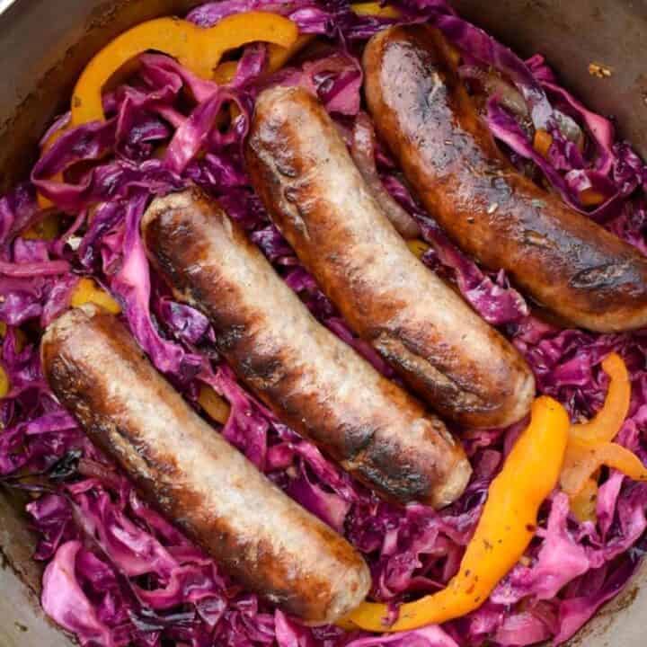 Bratwurst links nestled in purple cabbage and orange bell pepper strips