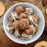 A white bowl full of apple pie energy balls coated in white chocolate drizzle