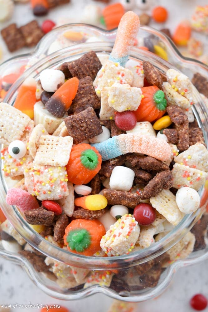 Overhead shot of colorful Halloween puppy chow in a glass pumpkin on a white wooden background