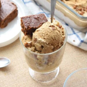 A glass dish full of scoops of gingerbread ice cream and topped with a wedge of soft gingerbread