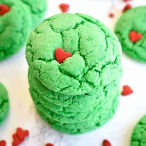 A stack of vibrant green Grinch cookies with red heart sprinkles