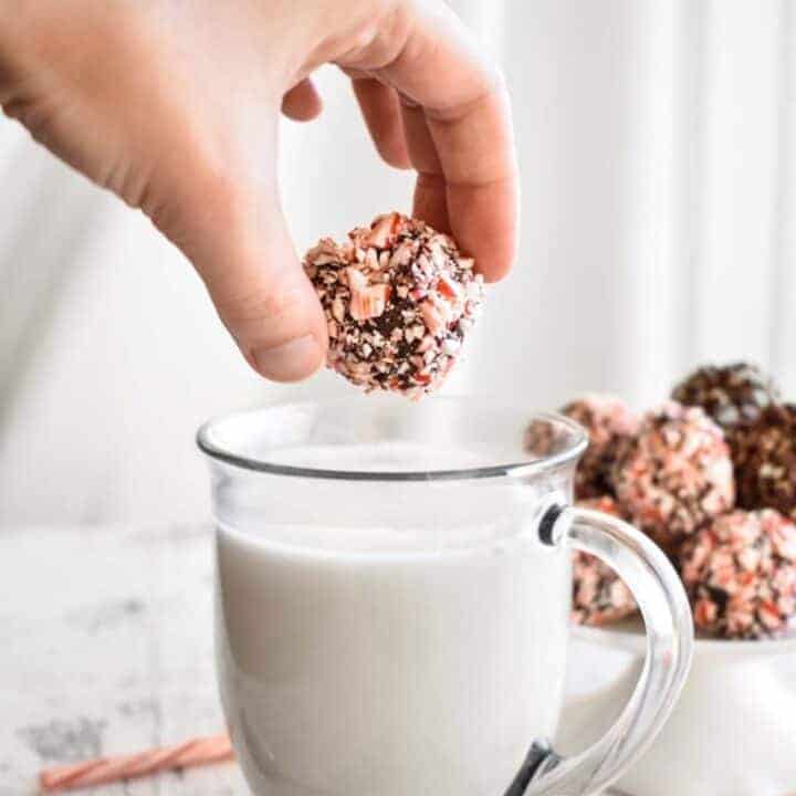 Peppermint Hot Chocolate Truffle Bomb being held above a clear mug of hot milk