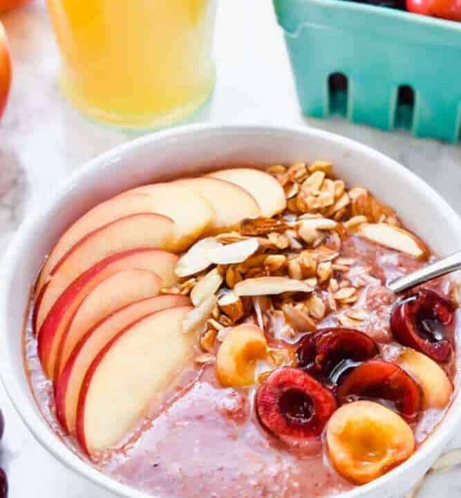 Apple Cheery Smoothie Bowl on a table with fresh fruit and orange juice