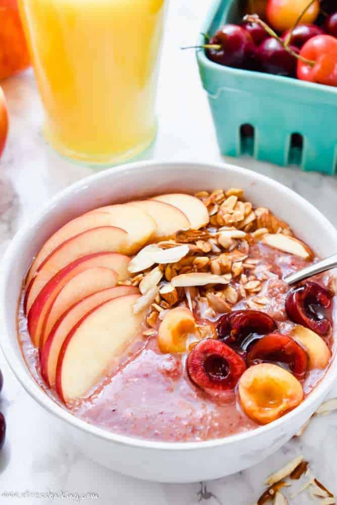Apple Cherry Smoothie Bowl on a table with fresh fruit and orange juice