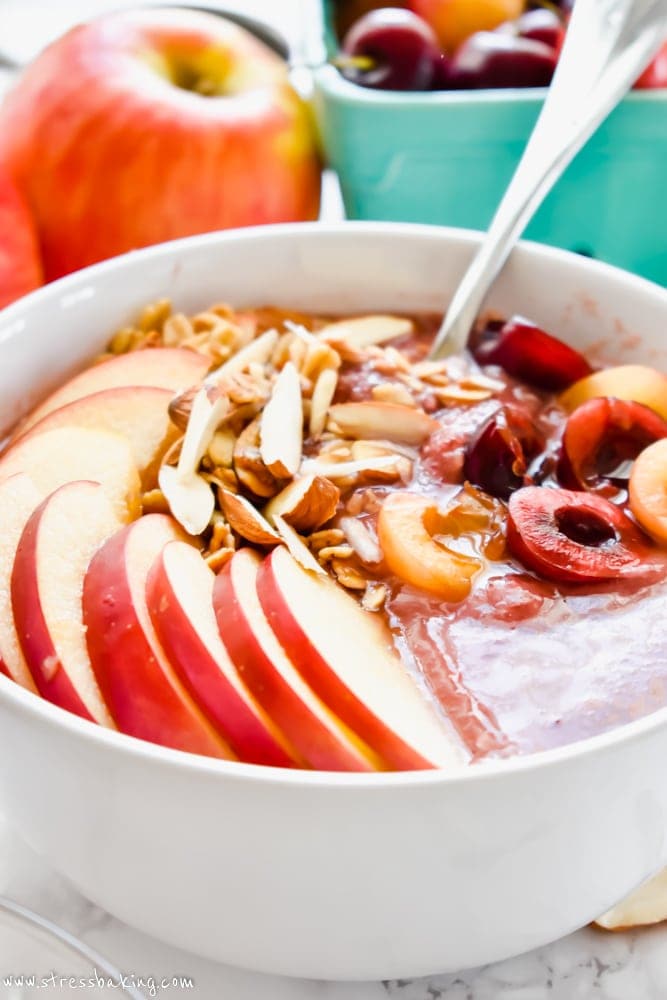 Closeup of smoothie bowl topped with sliced apples, cherries and nuts