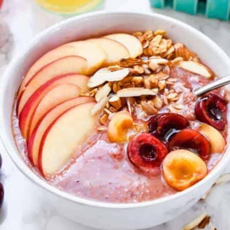 Pink smoothie bowl on a table with fresh fruit and orange juice