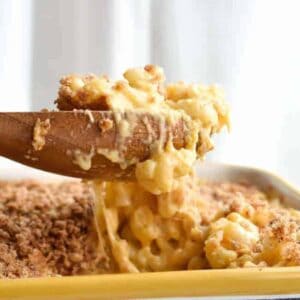 Wooden spoon lifting melty baked mac and cheese out of a dish