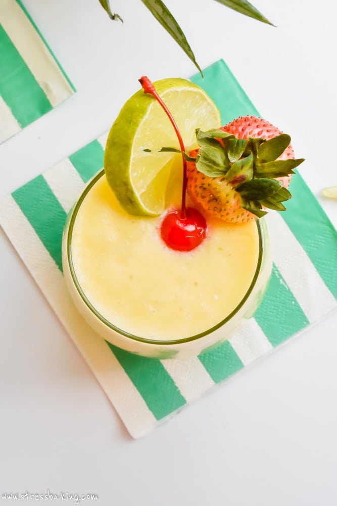 Pineapple cooler summer cocktail with lime, strawberry and a maraschino cherry on a napkin