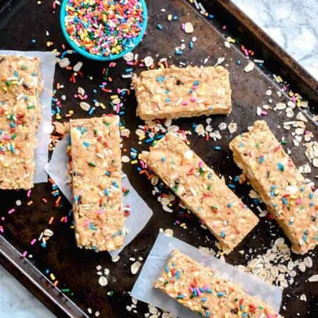 Chewy Funfetti Granola Bars on a baking sheet surrounded by colorful sprinkles