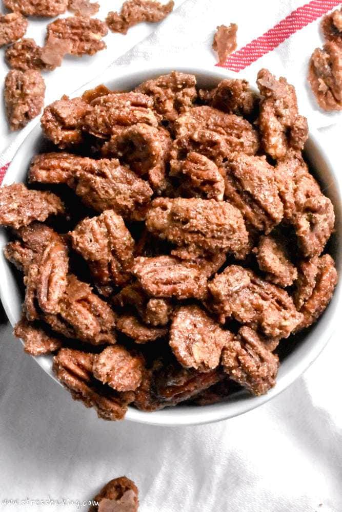 Overhead shot of candied pecans piled into a white bowl on top of a white dishcloth