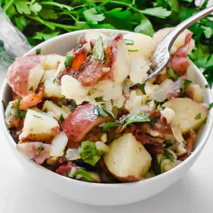 A forkful of German potato salad in a white bowl
