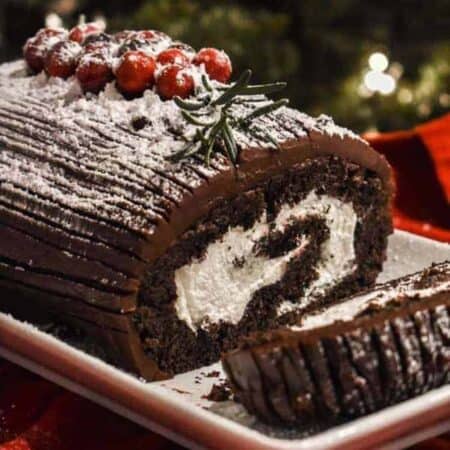 Yule Log Cake on a white platter with a slice on its side