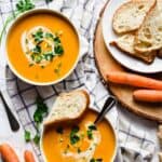 Two bowls of bright orange soup in white bowls with bread