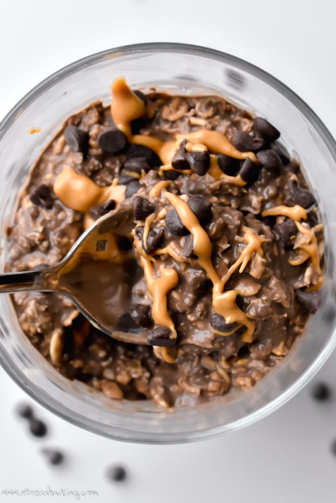A spoonful of chocolate and peanut butter overnight oats held over a glass jar
