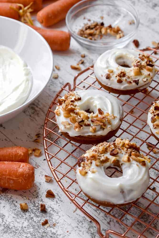 Carrot cake donuts topped with cream cheese icing and chopped nuts on a gold wire rack