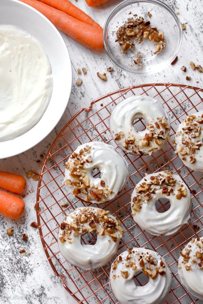 Overhead shot of carrot cake donuts topped with cream cheese icing and chopped nuts on a gold wire rack